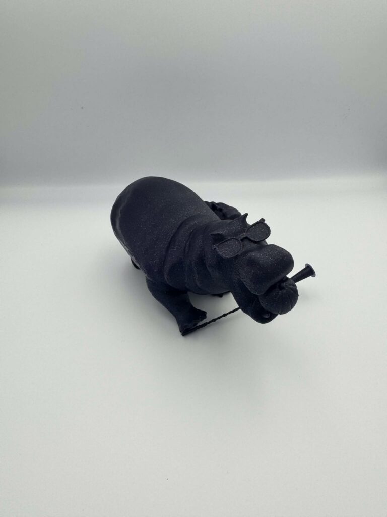 A black 3D-printed hippopotamus model has a rounded body, small glasses and a playful object held in its mouth.