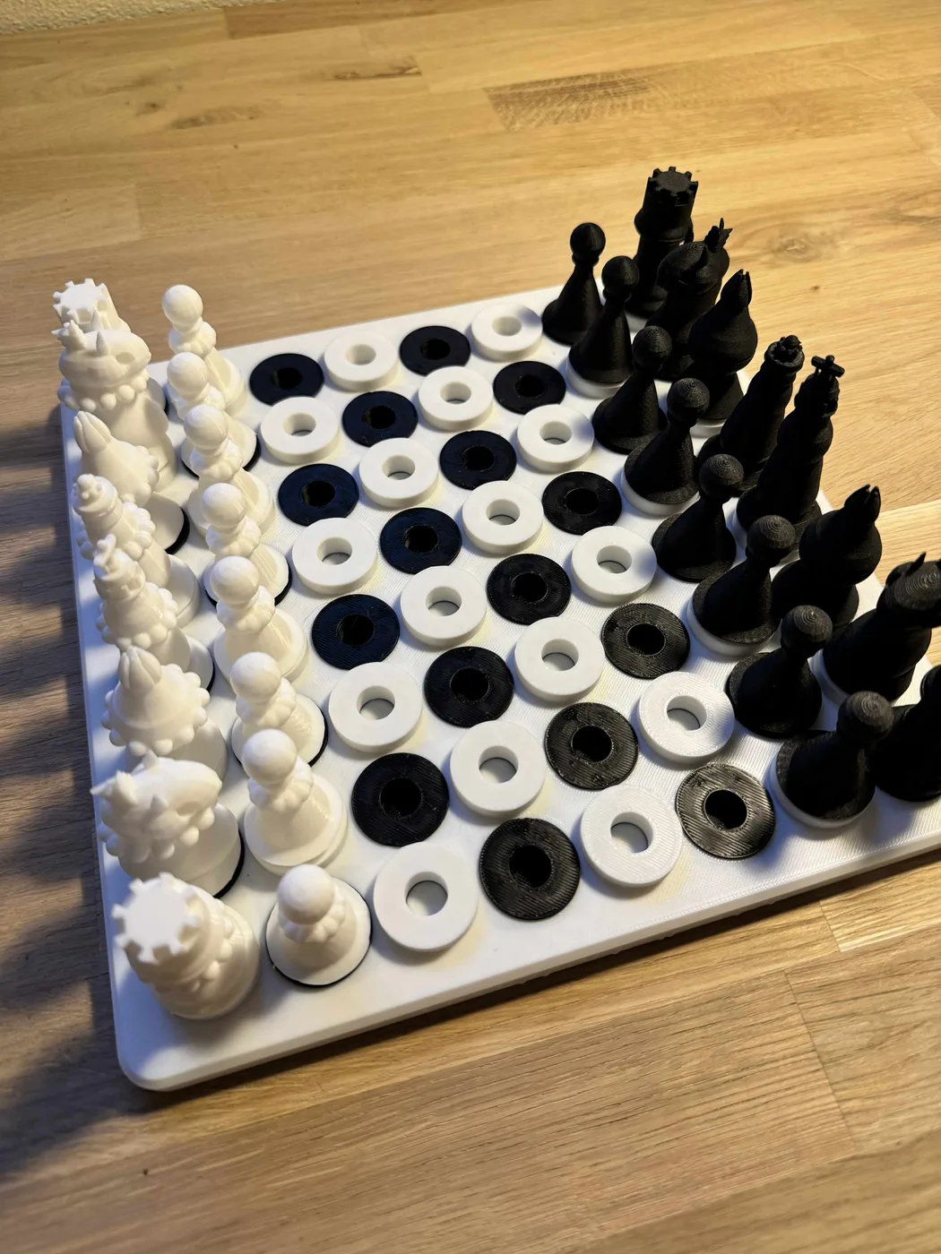 An accessible 3D-printed chess set is arranged in starting position on a tactile peg-in-hole chess board, with white pieces marked by raised sphere rings and smooth black pieces for touch distinction.