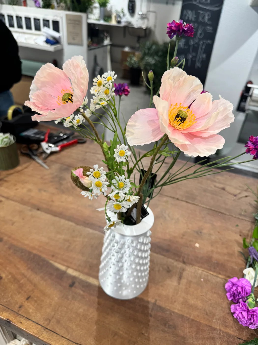 A 3D-printed Fibonacci vase with a white textured surface sits on a wooden table holding a colourful spring bouquet.